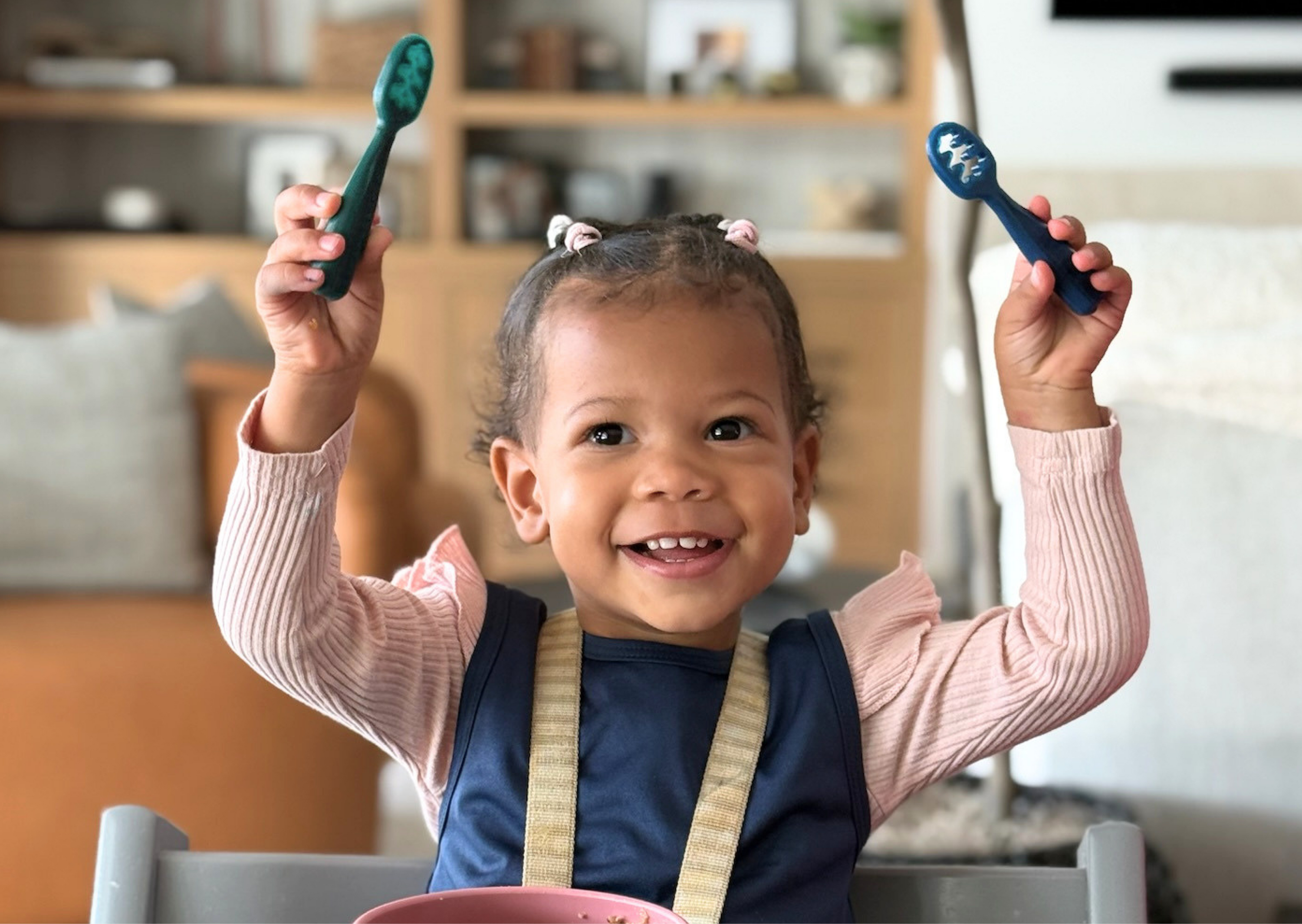 Child holding two toothbrushes in a kitchen setting
